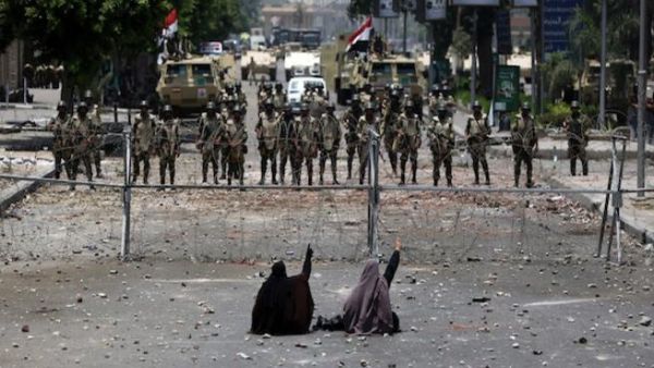 Two veiled Egyptian women, supporters of deposed president Mohamed Morsi, sit in front police standing behind barbed wire fencing that blocks the access to the headquarters of the Republican Guard in Cairo on July 8, 2013. (AFP)