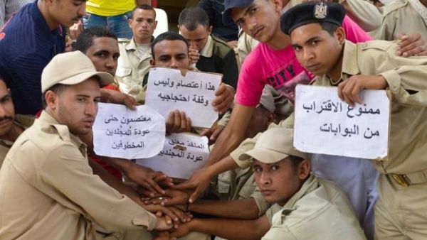 Egyptian police hold signs denoting that the gates are closed and demanding the return of their colleagues, as they gather at the Egyptian crossing point into the Gaza Strip (Mohamed el-Shahed/ AFP)