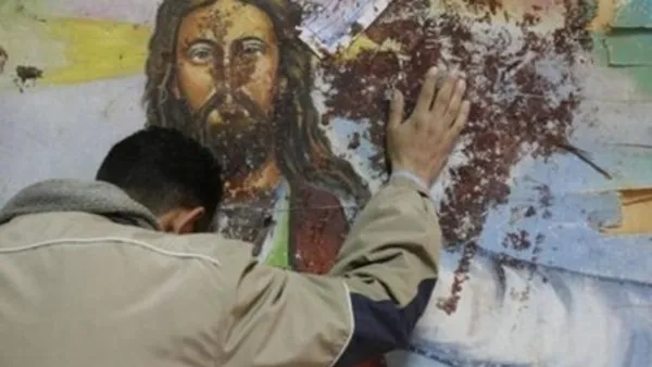 مصري قبطي يستند الى جدار عليه صورة المسيح وقد لطخته الدماء اثر اعتداء كنيسة القديسين