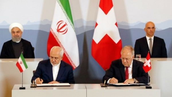 Iranian President Hassan Rouhani (top- L) and Swiss President Alain Berset (top-R) watch as Iranian Foreign Minister Mohammad Javad Zarif (L) and Swiss Economic Minister Johann Schneider-Ammann sign an agreement in Bern on July 3, 2018. (AFP)