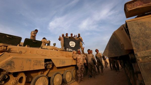 Members of the Iraqi forces pose for a photograph with a Daesh flag (Safin Hamed/AFP)