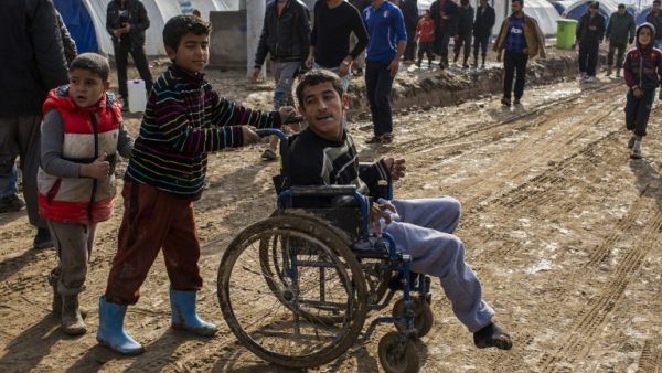 Children help a disabled young man at al-Khazer refugee camp near the Kurdish checkpoint of Aski kalak, 40 km West of Erbil on December 21, 2016. (AFP/JM Lopez)