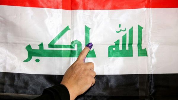 An Iraqi woman shows her ink-stained index finger before a national flag after having cast her vote in the country’s parliamentary election, in the capital Baghdad's Karrada district on May 12. (AFP)