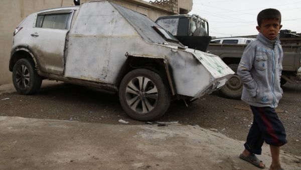An Iraqi boy walks by a car with defused bomb in a neighborhood recently secured by Iraqi security forces in western Mosul on April 2, 2017, during the retake of the city from Daesh fighters. (AFP/Ahmad Gharabli)