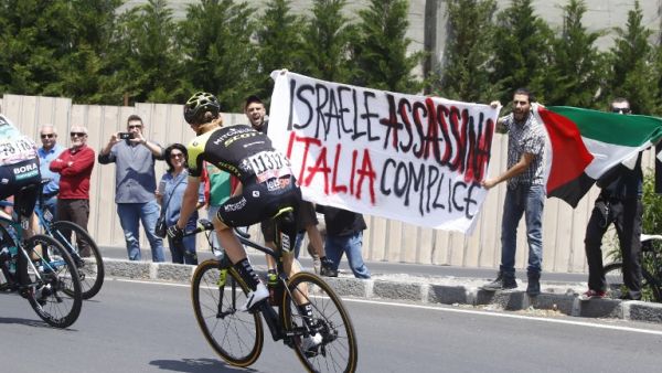 Australia's rider of team Mitchelton-Scott Jack Haig rides past protesters holding a banner reading "Israel assassinate, Italy complicit" before the start of 4th stage between Catania and Caltagirone (Sicily) of the 101st Giro d'Italia, Tour of Italy cycling race, on May 8, 2018 in Catania. (Luk Benies, AFP/File Photo 
