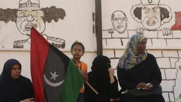 ليبيات يجلسن بالقرب من رسومات للعقيد الليبي معمر القذافي في بنغازي