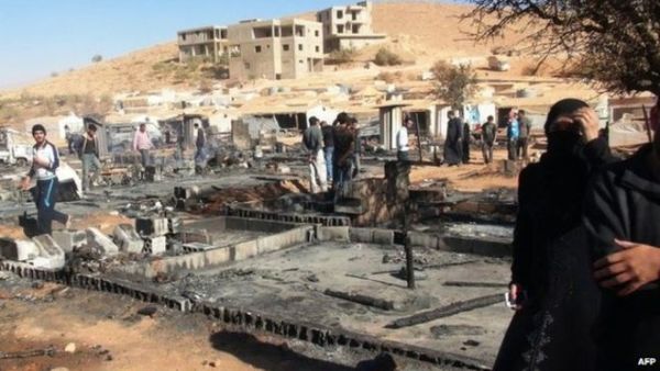 People walk past the charred remains of tents at a refugee camp outside Arsal, Lebanon. (AFP)