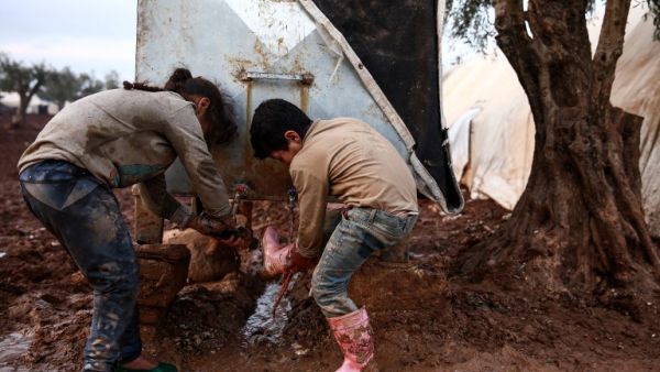 A Syrian boy and girl wash their boots and shoes from a cistern at a camp for the displaced near the village of Shamarin, near the border with Turkey. (AFP)
