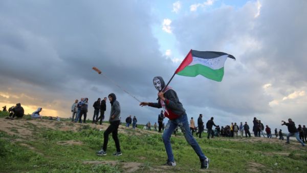 A Palestinian protester wearing a Guy Fawkes mask while holding a Palestinian flag and hurling a slingshot following a demonstration at Gaza border with Israel. (SAID KHATIB / AFP)