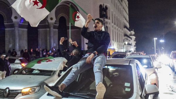 An Algerian youth waves a national flag as he sits atop a car during a demonstration in the centre of the capital Algiers on March 11, 2019, after President Abdelaziz Bouteflika announced his withdrawal. (AFP)