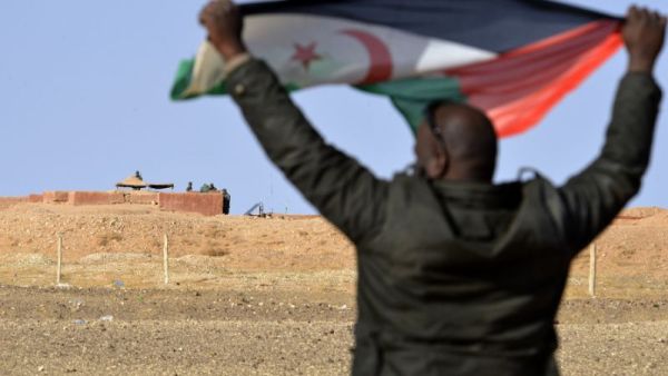 A Saharawi holds up a Polisario Front flag in Al-Mahbes area near Moroccan soldiers guarding the wall separating the Polisario-controlled Western Sahara from Morocco. (AFP Photo/STRINGER)