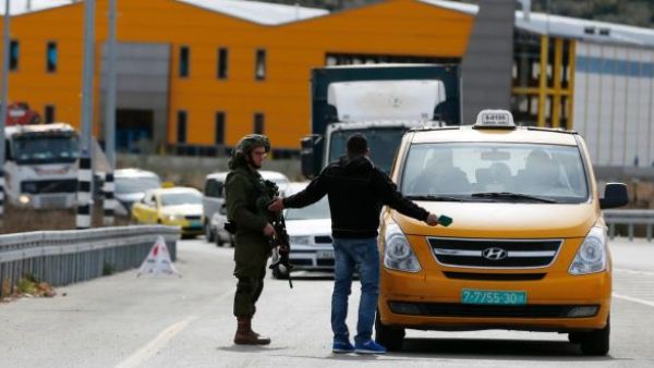 An Israeli soldier checks the documents of a Palestinian passenger of a taxi. (AFP/File)