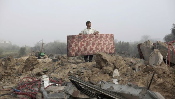 A Palestinian man carries a mattress at the rubble of a destroyed building following a military attack on his home. (AFP/File)