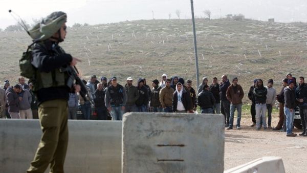 An Israeli soldier stands guard next to Palestinian workers who were transported out of the Tekoa settlement south of Jerusalem following a terror attack in the community on January 18, 2016. (AFP/Menahem Kahana)