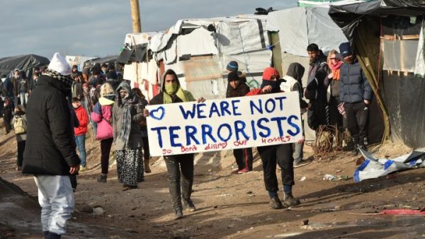 Refugees hold a sign reading “we are not terrorists” during the dismantling of the “jungle” refugee camp in Calais, France, in February 2016. (AFP/Philippe Huguen)