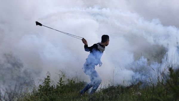 A Palestinian protester uses a slingshot to throw a tear gas canister back during clashes with Israeli security forces. (AFP/File)