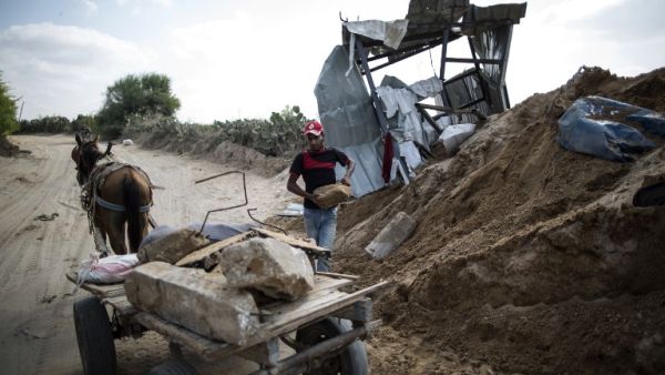 A Palestinian man loads stones on a cart next to a crater on August 22, 2016 in Beit Lahia in the northern Gaza Strip, following an Israeli airstrike the day before. (AFP/Mahmud Hams)