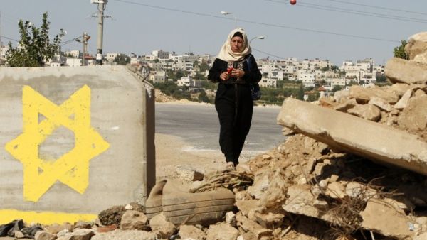 A Palestinian woman passes a roadblock, on which a star of David is painted, on July 10, 2016 in the West Bank village of Sair, east of Hebron, as the IDF keeps the area under lockdown after an Israeli man was shot and wounded near the Tekoa settlement. (AFP/Hazem Bader)