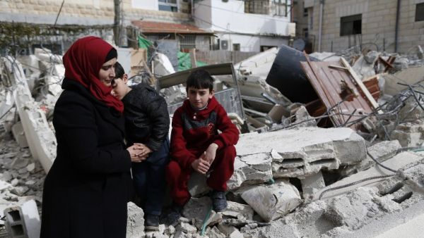 Palestinian children and their mother sit on the rubble of their house that was demolished by Israeli army bulldozers in the east Jerusalem neighborhood of Beit Hanina on February 22, 2017. (AFP/Ahmad Gharabli)