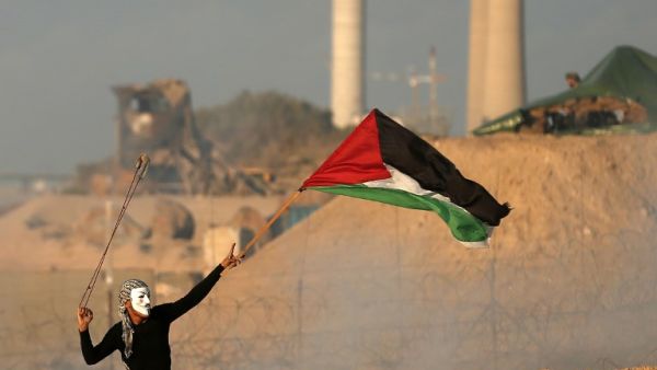 A masked Palestinian protester carries a national flag as he hurls stones during a demonstration calling for an end to the Israeli blockade on Gaza. (MAHMUD HAMS / AFP)