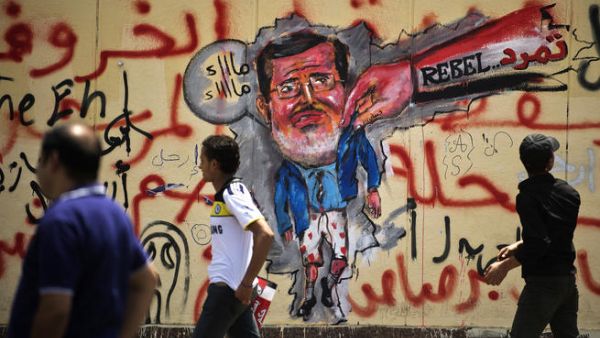 Egyptian protesters walk past graffiti against President Mohamed Morsi on the wall of the presidential palace in Cairo on July 1, 2013. (Source: AFP/GIANLUIGI GUERCIA)