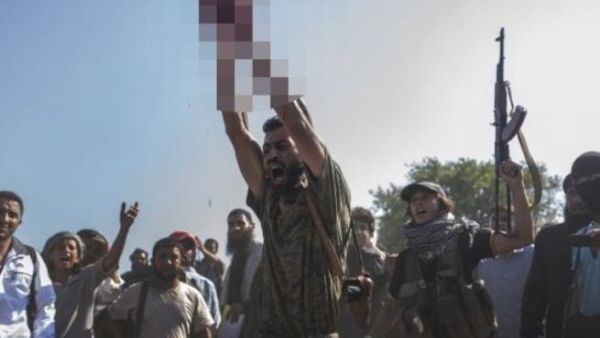 An ISIS soldier, in a recent execution, holds the severed head of a militant. [LeJournal]