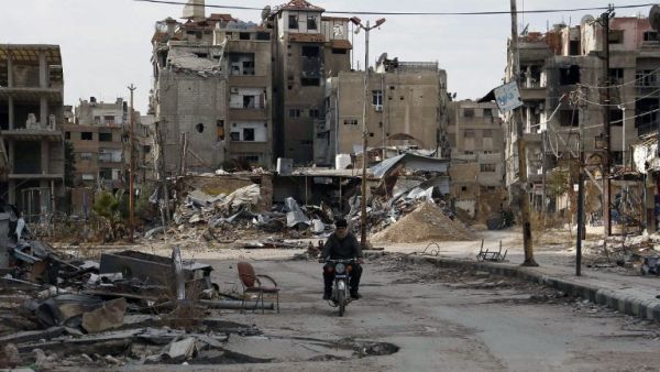 A man drives his motorbike past damaged buildings on February 10, 2016 in Harasta, east of the Syrian capital Damascus. (AFP/Abdulmonam Eassa)