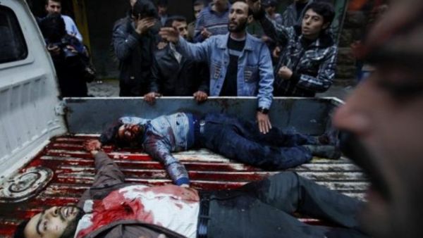 سوريون يحطيون بشاحنة صغيرة تحمل جثث مواطنيين قتلوا في قصف مدفعي على بستان القصر/أ.ف.ب