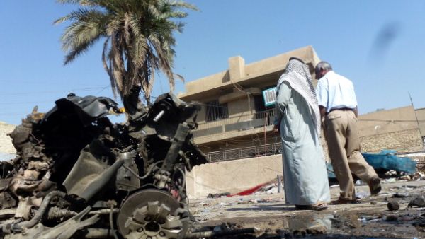 Iraqis look at the remains of a vehicle following an explosion on October 27, 2013, in the the Mashtal district of the capital Baghdad. [SABAH ARAR/AFP/Getty Images]