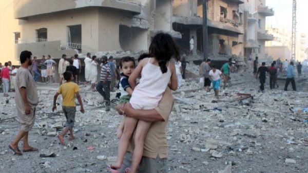 سوري يحمل طفليه مبتعدا عن مكان انفجار في مدينة الرقة/أ.ف.ب