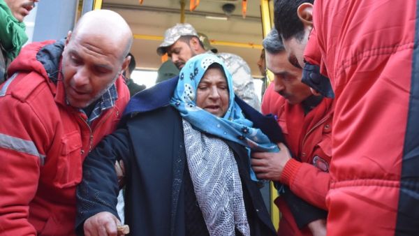 A woman is assisted by members of the Syrian Arab Red Crescent after two buses evacuated civilians from Fuaa and Kafraya, two Shia villages under rebel-siege near Idlib, on December 19, 2016. (AFP/George Ourfalian)