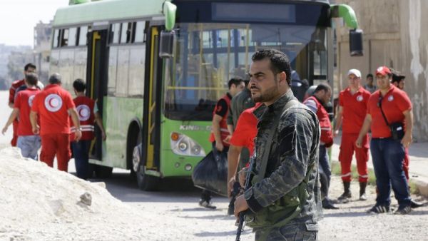 A Syrian soldier stands guard as Red Crescent members wait for opposition fighters and their families to change buses at a Syrian army checkpoint on the edge of the rebel-held Waer neighbourhood in the central city of Homs during an evacuation operation on September 22, 2016. (AFP/Louai Beshara)