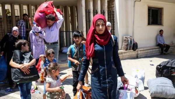 Syrian refugees asnd children walk with their belongings as they prepare to board a bus at the Masnaa crossing on the Lebanon-Syria border on July 28, 2018, returning them back to Syria. (AFP/ Photo)
