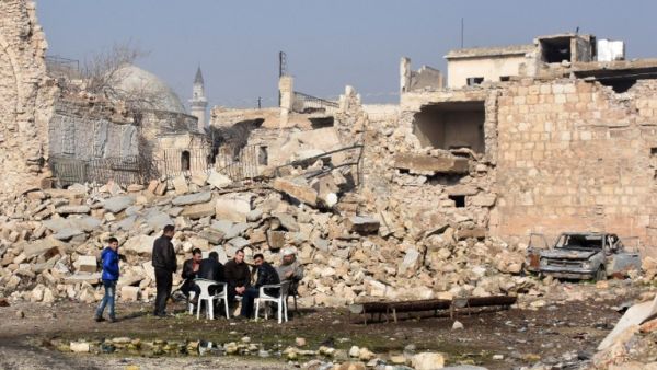 Syrians sit in the street on front of a destroyed building in Aleppo's old city on January 19, 2017, a month after government forces retook the northern Syrian city from rebel fighters. (AFP/George Ourfalian)