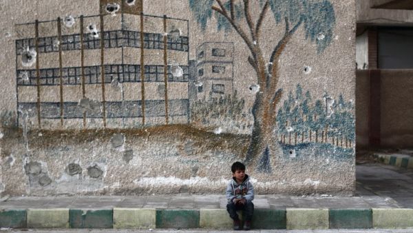 A Syrian child sits in front of a mural covered in bullet holes in Eastern Ghouta, on the outskirts of Damascus. (AFP/Abdulmonam Eassa)