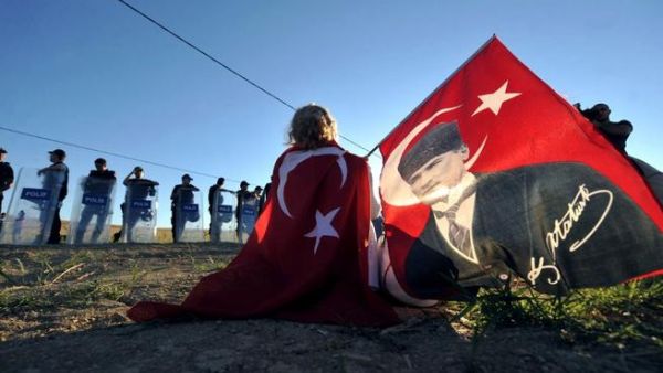 TURKEY, Silivri : Wrapped in a Turkish flag and holding another one with a portrait of Mustafa Kemal Ataturk, a protestor sits in front of police forces blocking the access to a courthouse in Silivri, near Istanbul, on August 5, 2013, where Ilker Basbug was sentenced to life imprisonment. AFP PHOTO / OZAN KOSE TURKEY, Silivri : Wrapped in a Turkish flag and holding another one with a portrait of Mustafa Kemal Ataturk, a protestor sits in front of police forces blocking the access to a courthouse in Silivri, near Istanbul, on August 5, 2013, where Ilker Basbug was sentenced to life imprisonment. AFP PHOTO / OZAN KOSE