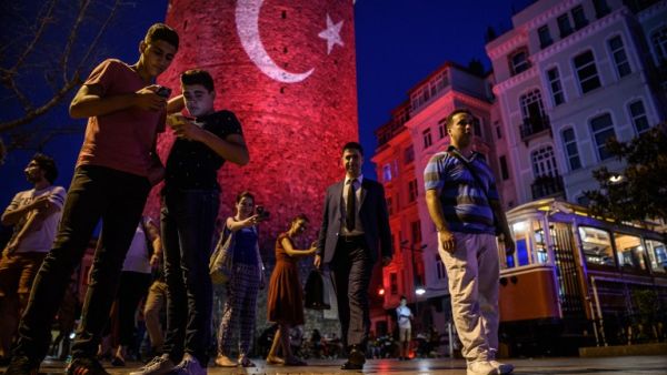 People take pictures on a street near the Galata Tower, illuminated in Turkish flag colors on August 1,2016 at Galata district in Istanbul. (AFP/Ozan Kose)
