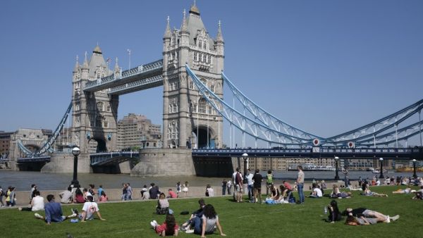 People relax in the hot and sunny weather on the grass beside Tower Bridge and the river Thames in London on May 26, 2017. (DANIEL LEAL-OLIVAS / AFP)