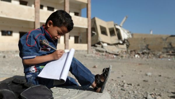 A Yemeni boy school writes as he sits outside a school on March 16, 2017, that was damaged in an air strike in the southern Yemeni city of Taez. (AFP/Ahmad al-Basha)