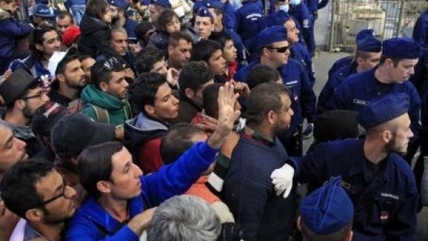 أفراد من الشرطة المجرية يراقبون مهاجرون يصطفون للصعود إلى القطار في بودابست يوم الأربعاء
