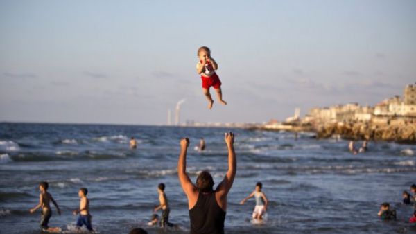 In a moment of calm following 2014's brutal war in Gaza, a man throws his laughing baby into the air on the beach in Gaza City.  Gaza's beaches, where last summer four boys were killed by Israeli missiles while playing soccer, are worlds away from the swanky seaside hangouts of Tel Aviv.  (AFP/Mahmud Hams)