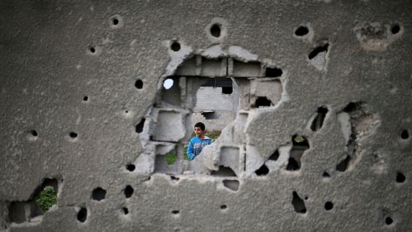 A Palestinian boy stands behind a bullet-ridden wall in Gaza City, destroyed during 2014's month-long war between Israel and Hamas militants, which devastated Gaza's civilians. (AFP/Mohammed Abed)