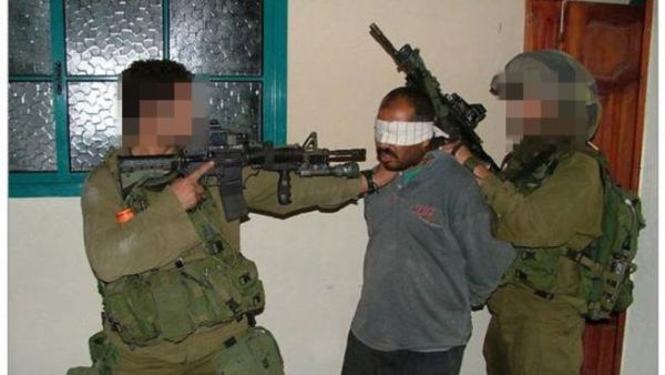 صورة لجندي اسرائيلي يوجه بندقيته الى وجه فلسطيني مكبل ومعصوب العينين داخل منزله في غزة