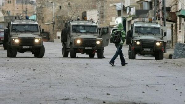 فتى فلسطيني يمر امام مدرعات اسرائيلية في الخليل في الضفة الغربية
