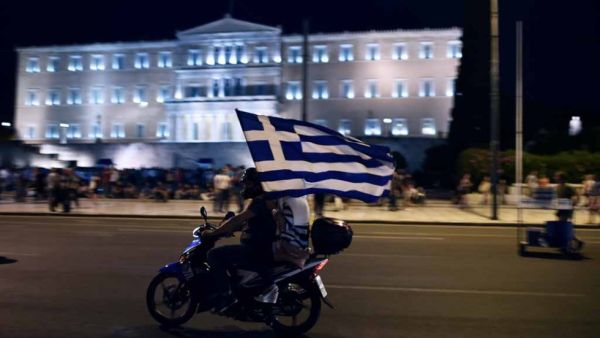 A motorcylist with his passenger holding a Greek flag passes in front of the Greek Parliament (AFP/File Photo)	