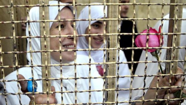 Egyptian women members of the Muslim Brotherhood hold roses as they stand in the defendants' cage dressed in prison issue white during their trial in at the court in the Egyptian Mediterranean city of Alexandria on December 7, 2013. [Getty Images]