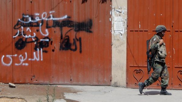 A Lebanese soldier walks past anti-Assad graffiti in the northern city of Tripoli (AFP)