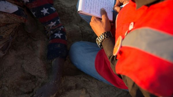 A member of the Libyan Red Crescent takes notes next to the body of a migrant on the beach in Qasr al-Garabulli, west of Tripoli, on March 20, 2016. (AFP/Stringer)