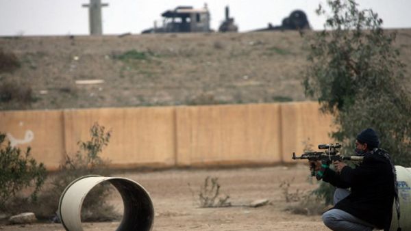 An armed Iraqi holds his rifle, as he looks towards a burnt out lorry seen at the side of the main highway leading west out of the capital Baghdad to the city of Fallujah, in Anbar province, on January 5, 2014. [AFP]