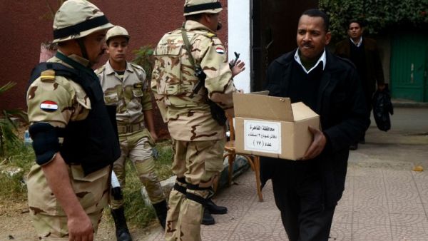 A man carries a box full of voting ballots near Egyptian soldiers standing guard outside a school that will be used as a polling station on January 13, 2014 in Cairo. [AFP]